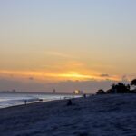 a beach with people walking on it at sunset
