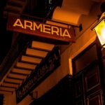 A store sign reads "armeria" lit by a lantern.